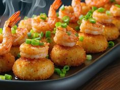 shrimp and scallops on a black plate with steam rising from the top, along with green onions