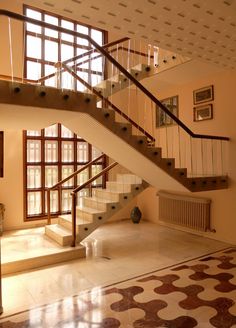 a staircase in the middle of a living room with tile flooring and large windows