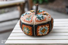 a small crocheted pumpkin sitting on top of a wooden table next to a bench