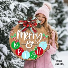 a woman holding a merry and bright sign in front of snow - covered pine trees