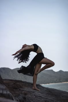 a woman standing on top of a rock next to the ocean with her arms stretched out