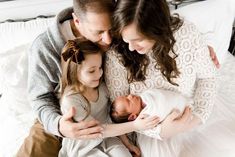 a man and woman holding a baby in their arms while sitting on a white bed