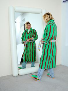 two women in green and red striped robes looking at themselves in a large white mirror