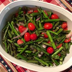 a white bowl filled with asparagus, tomatoes and onions on top of a checkered table cloth