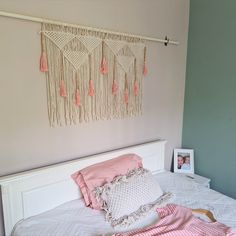 a white bed topped with pink pillows next to a wall hanging over it's headboard