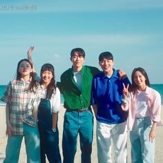 a group of people standing next to each other on top of a sandy beach with the ocean in the background