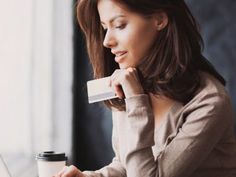 a woman sitting in front of a laptop computer holding a business card and looking at the screen