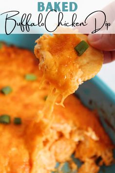 a hand holding up a piece of baked buffalo chicken dip from a blue casserole dish