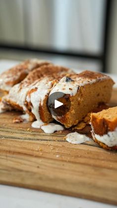 a wooden cutting board topped with pieces of cake covered in icing and marshmallows