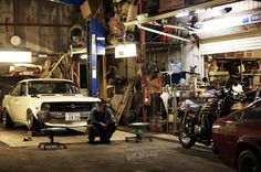 a man sitting on the ground next to a car in a garage with other cars