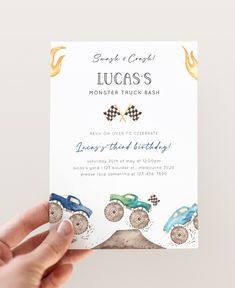 a person holding up a birthday card with two monster trucks on it and the words lucas's monster truck bash