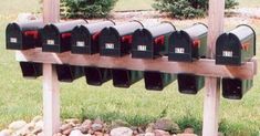 a row of mail boxes sitting on top of a wooden pole next to rocks and grass