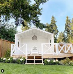 a small white house sitting on top of a lush green field next to a wooden fence