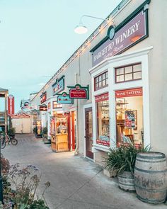 an empty street in front of a winery with wine barrels on the sidewalk and lights hanging above it