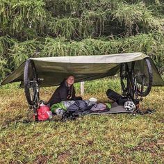 a man sitting in the grass under a tent with his bike attached to it's side