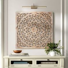 a white table topped with a vase filled with flowers and a wooden cutout on the wall