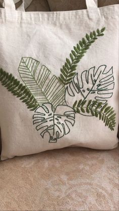 a white bag sitting on top of a couch next to a pillow with green leaves