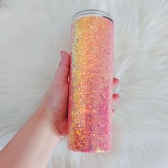 a hand holding a pink and yellow glitter tumbler cup on top of a white rug