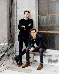 two young men sitting on a bench in front of a window with their arms crossed