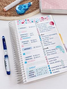 an open planner next to a pen and some other items on a white table with a straw hat