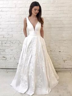 a woman standing in front of a brick wall wearing a white wedding dress with deep v - neck