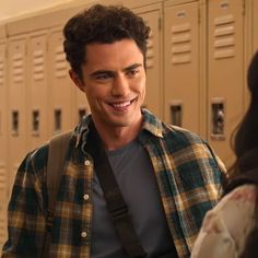 a man standing in front of lockers with a smile on his face and wearing a backpack