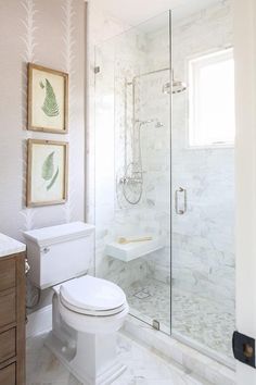 a white toilet sitting next to a walk in shower under a bathroom window with two paintings on the wall