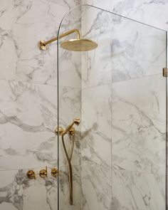 the shower head is mounted to the wall in this bathroom with marbled walls and gold fixtures