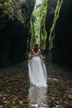 a woman standing in the middle of a river wearing a white dress and flowing water