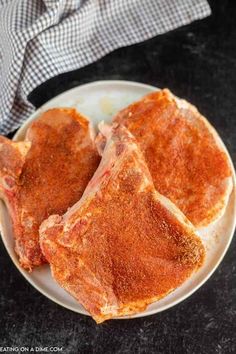 two pieces of meat on a white plate with a blue checkered napkin in the background