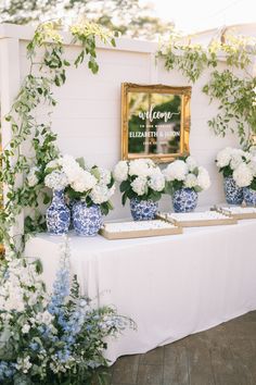 blue and white vases with flowers on a table in front of a framed sign