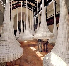 a man is standing in front of some tall white sculptures that are hanging from the ceiling