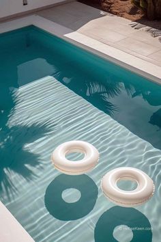 two inflatable floats floating on top of a swimming pool next to a palm tree