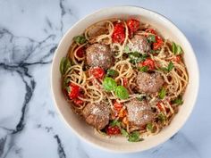 a white bowl filled with pasta and meatballs on top of a marble countertop