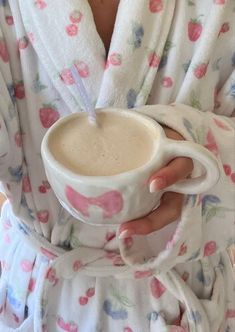 a woman is holding a cup of coffee in her hand and wrapped in a robe