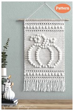 a crocheted wall hanging with beads and tassels on the bottom, in white