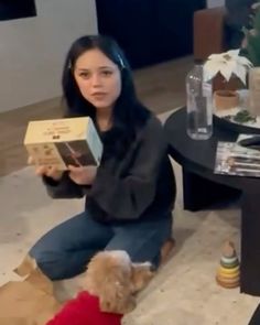 a woman is sitting on the floor reading a book with her dog beside her,