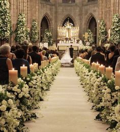 the aisle is lined with flowers, candles and greenery as well as people sitting in pews