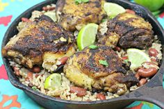 a skillet filled with rice and meat covered in lime wedges on top of a colorful table cloth