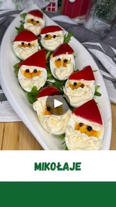 a white plate topped with deviled eggs covered in santa claus's hats and green leaves