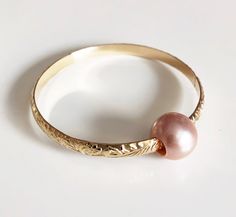 Adorable heirloom bangle for your princess is make with decorative floral pattern wire and genuine pink Edison pearl. Bangle is hand- formed, hammered and polished for a stunning texture and shine. It looks great worn alone or paired with other shell and charm bangles to create a chic, fun beachy look. Pink Edison pearl is 10-11 mm. Bangle is about 4mm wide and 1.5 in thickness. For engraving inside bangle: https://etsy.me/2H0W6C3 As you can see in the photos there are naturally occurring blemis Pink Round Heirloom Jewelry, Elegant Pink Pearl Bangle Bracelet, Delicate Pink Pearl Bracelet For Wedding, Delicate Pink Round Bracelets, Elegant Pink Gold Bangle As Gift, Elegant Pink Bangle Jewelry, Pearl Bangle As Gift, Pink Pearl Charm Jewelry For Wedding, Elegant Handmade Hoop Bracelet