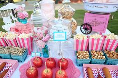 a table topped with lots of food next to a pink tray filled with apples and hotdogs