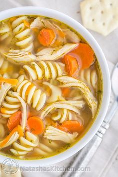 a bowl of chicken noodle soup with carrots and crackers on the side