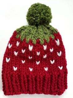 a red knitted hat with white hearts on the side and a green pom - pom