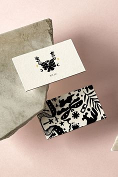 two business cards sitting next to each other on top of a pink surface with white and black designs