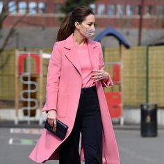 a woman walking down the street wearing a pink coat and black pants with a face mask on