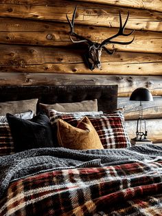 a bed with plaid blankets, pillows and a deer head mounted on the wall