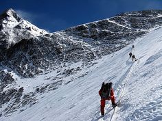 three people walking up the side of a snow covered mountain