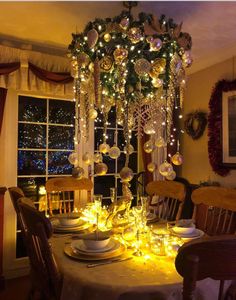 a dining room table set for christmas with lights and ornaments hanging from the chandelier