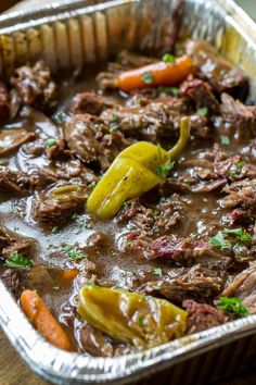 beef stew with carrots, peppers and parsley in a metal pan on a wooden table